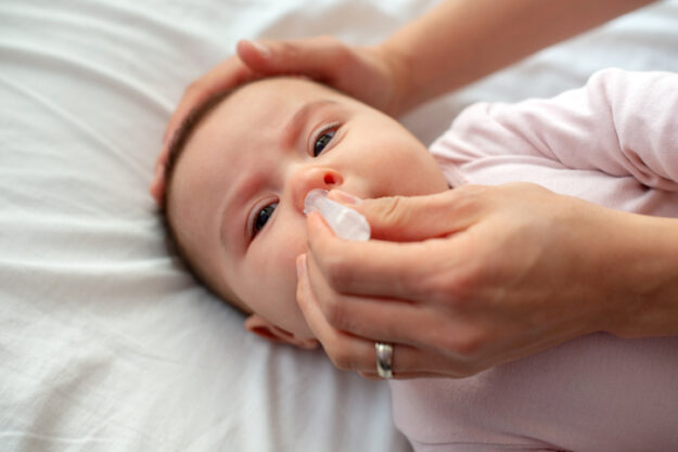 Close up of caring  mother with nasal pump to clean her baby’s nose. Baby lying in bed